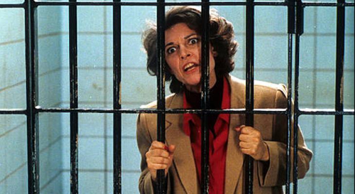 A woman standing in a jail cell holding onto the bars