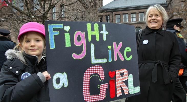 a girl and a woman hold a sign at a protest that says fight like a girl