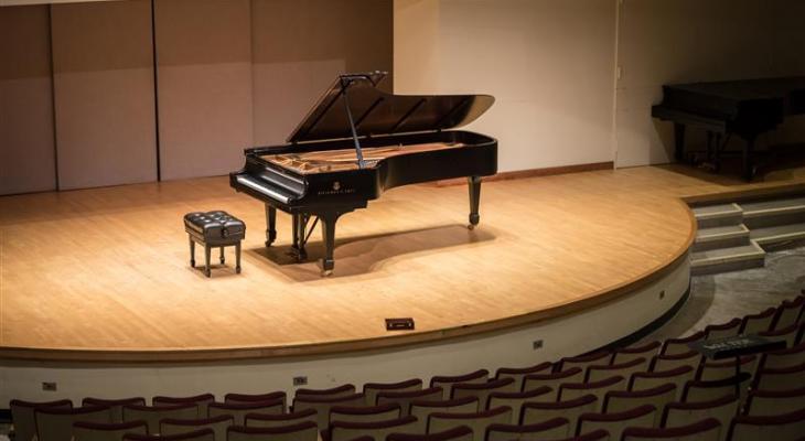 A grand piano sits in the spotlight on the Walter Hall stage surrounded by empty seats.