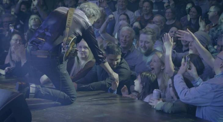 A member of the band reaches down to greet a fan in the audience.