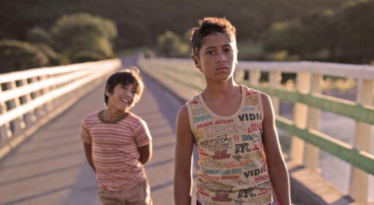 Two boys cross a bridge, walking towards the camera.