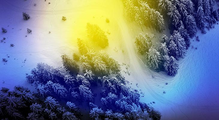 An aerial view of a field and evergreens covered with snow with a blue and yellow aura filter.