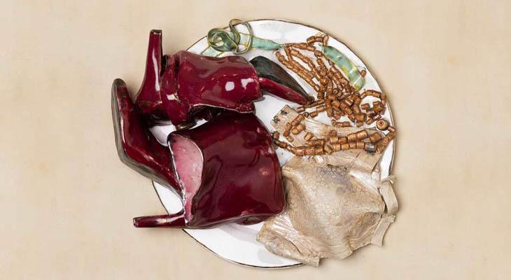 A ceramic sculpture of a dinner plate with red boots, a nude bra, a necklace, and other accessories