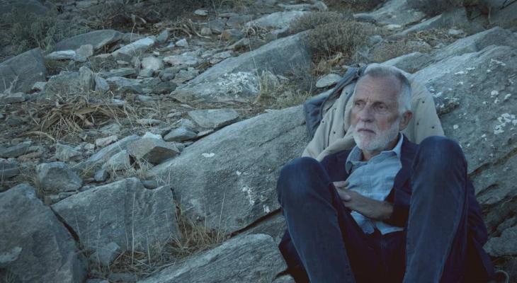 a man with a beard sitting next to a large rock