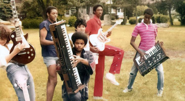a group of people playing with guitars and synthesizers in a park
