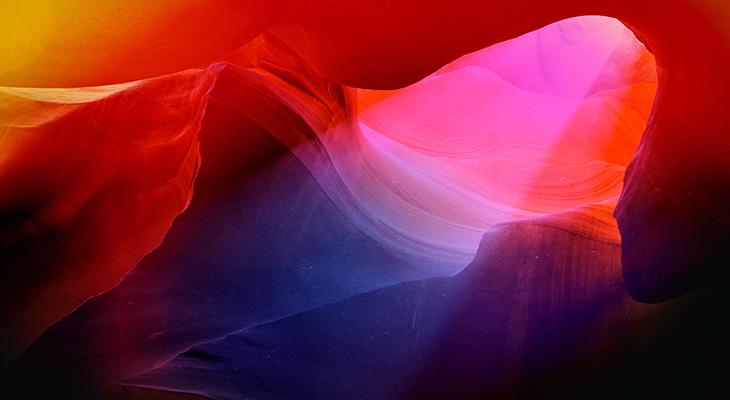 A colourful aura photograph with splashes of blue, pink, orange and black, of Antelope Canyon with a beam of light shining down.