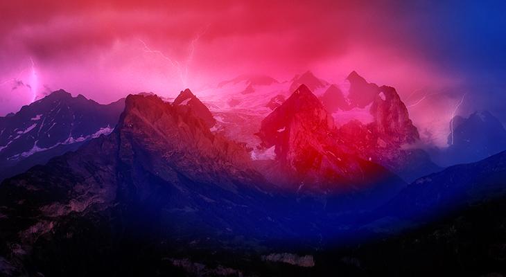 A wide landscape image of a jagged mountain range under a cloudy sky as lightning bolts strike the ground