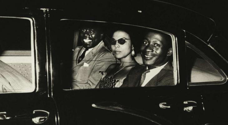 Patrice Lumumba's speechwriter Andrée Blouin seated in the back of a limousine flanked by two men.