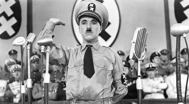 Charlie Chaplin in a military uniform saluting in front of microphones