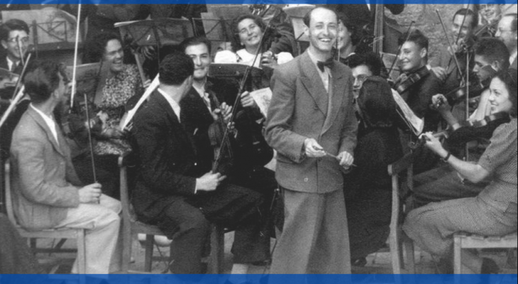 Black and white photograph of the Israel Philharmonic Orchestra. The conductor is smiling brightly while the orchestra members are seated with instruments in hand.