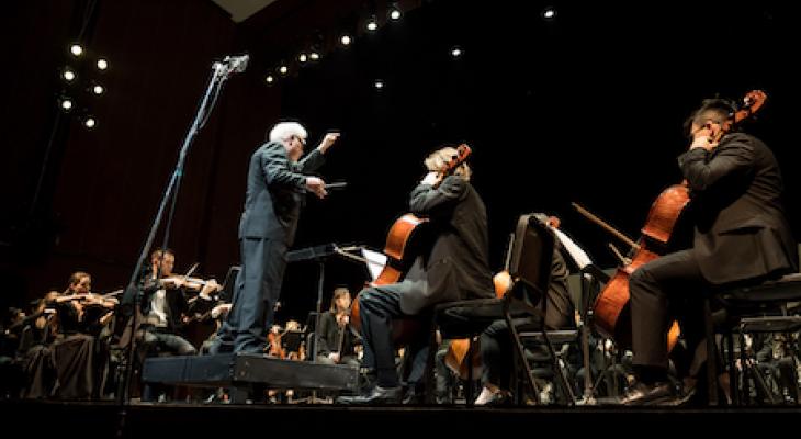 This picture shows a scene of a band rehearsing, with musicians gathered around the conductor in the middle of the stage.