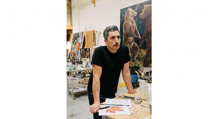 Artist Kent Monkman standing at a table in his studio.