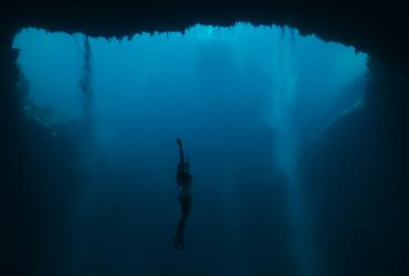 Floating in the depths of the ocean, a free-diver stretches her arms towards the surface.