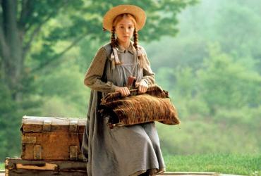 a young girl with braids and a wide brim hat sitting on a suitcase