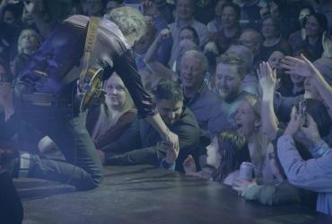 A member of the band reaches down to greet a fan in the audience.