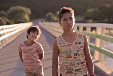 Two boys cross a bridge, walking towards the camera.