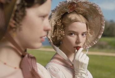 Two women in 19th-century dress. One of them eats a strawberry.