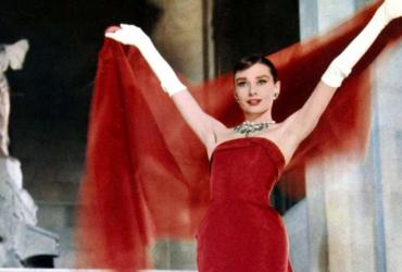 Audrey Hepburn models a red gown and chiffon cape.