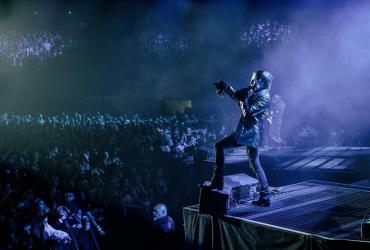 a man with extravagant makeup on singing on stage at a packed concert