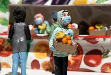 Polymer clay figures at a food bank. The figure in the foreground in holding a box with groceries and wearing a blue mask.