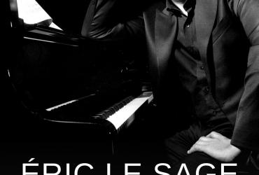 Éric Le Sage is sitting at the piano, looking at the camera and smiling.