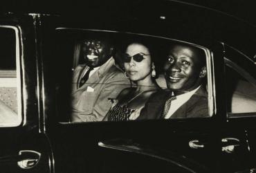 Patrice Lumumba's speechwriter Andrée Blouin seated in the back of a limousine flanked by two men.