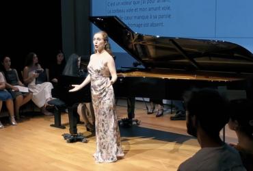 A singer is singing in the foreground with a grand piano behind her.