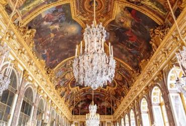 Hall of Mirrors at the Palace of Versailles during the day, featuring ornate painting ceiling, and grand chandeliers. 
