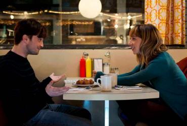 A young man and woman have a conversation at a booth in a diner.