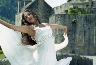 A woman dances in a wedding dress in front of a castle.