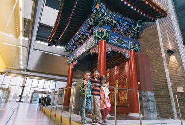 Three young children standing in front of a Chinese architecture entrance at ROM.