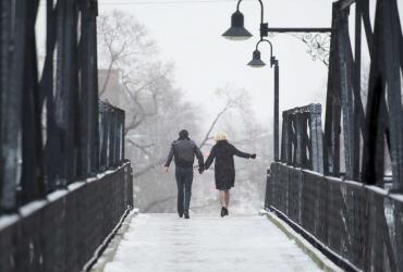 Holding hands, a man and a woman cross a bridge in the snow.